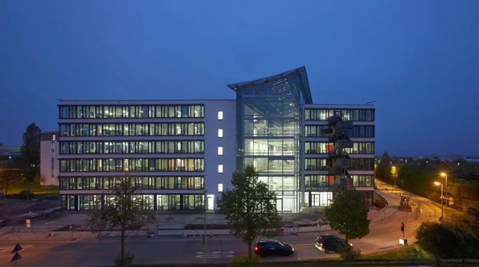 Fertiggestelltes Bürogebäude bei Nacht mit beleuchtetem gläsernem Atrium zwischen zwei Gebäudeflügeln
