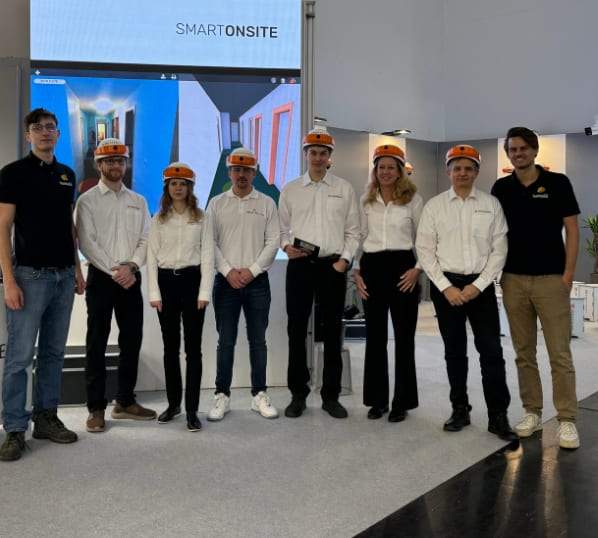 Das Team von Open Experience mit orangen DIGIBAU-Helmen am Messestand der BAU 2025