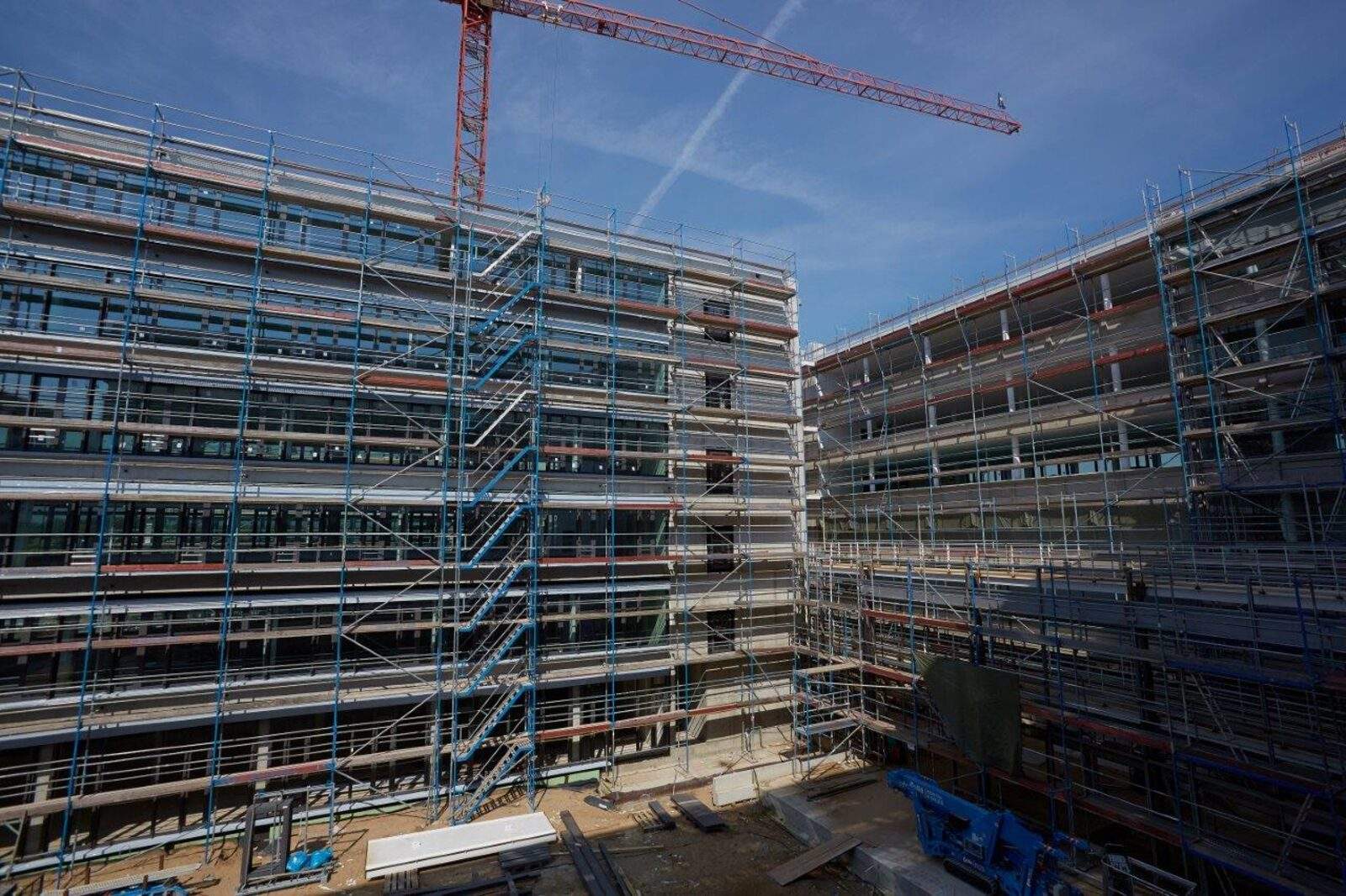 Innenhof eines eingerüsteten Verwaltungsneubaus, beide Gebäudeflügel mit gleichförmig wiederkehrenden Geschossbändern, Kran über dem Rohbau